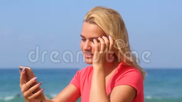 年轻漂亮的女孩在大海的背景上读短信视频的预览图
