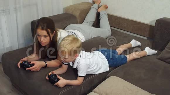 年轻的母亲和一个小儿子在家里的沙发上玩电脑游戏视频的预览图