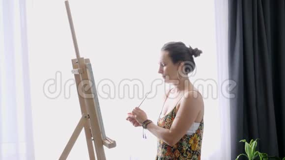 灵感来自年轻的女孩与薄刷在手画画布在艺术车间女艺术家正在画架上创作抽象画视频的预览图