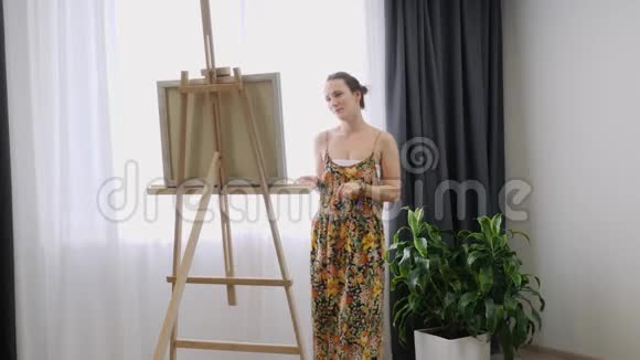 艺术家妇女站在画架上在画室里用丙烯酸颜料画画布视频的预览图