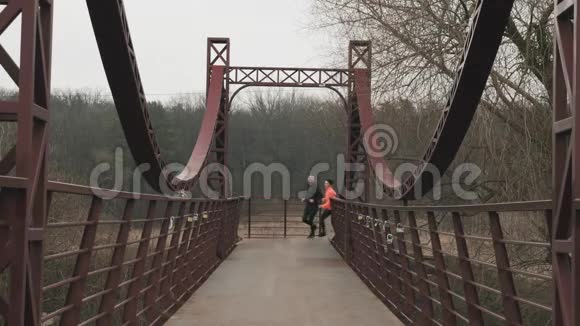 在公园里培养年轻夫妇活泼的年轻女子和男人正在穿过人行桥慢跑女性和男性视频的预览图