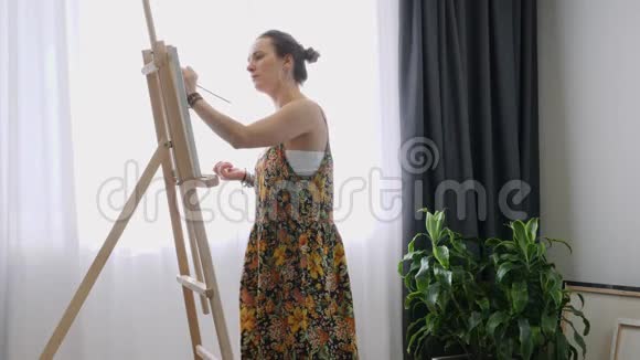 漂亮的女画家在画布上用薄薄的画笔作画美术家工作室画架上的帆布从事抽象工作的妇女视频的预览图
