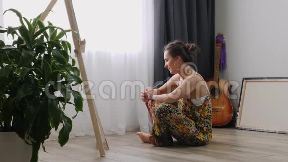 年轻漂亮的女人坐在家里的地板上拿着画笔在画布上画画艺术学院或绘画学校激励视频的预览图