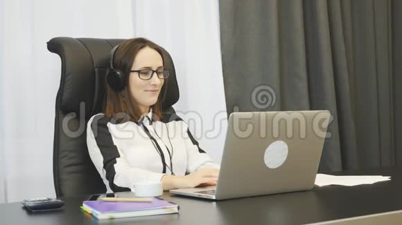 年轻的女办公室工作人员在工作场所听音乐耳机女商人坐在办公室听音乐视频的预览图