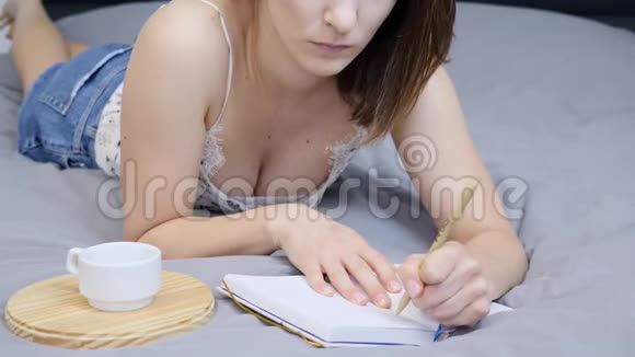 未被认出的白种人女人正在酒店房间的床上用笔记本做笔记美丽的女性正在写日记中的符号视频的预览图