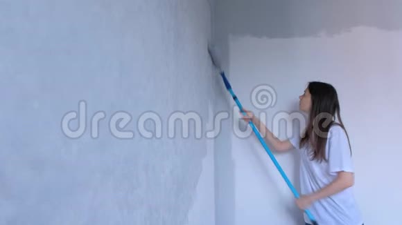 单身的年轻女孩画家是用平滚筒在灰色的墙壁上作画视频的预览图