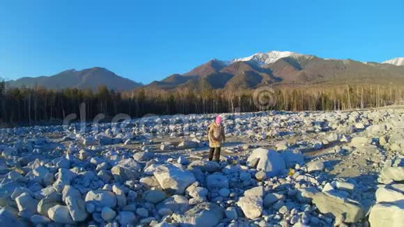 女孩穿过一片大石头的田野背景中的山景视频的预览图