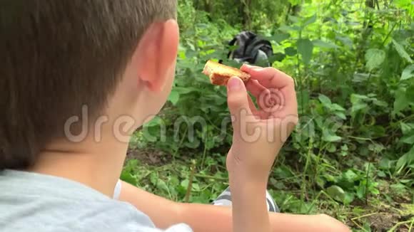 一位疲惫的饥饿男孩游客的肖像徒步旅行者正在森林里休息吃着饼干视频的预览图