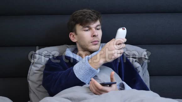 年轻男性使用遥控器打开空调肖像穿浴袍的男人在床上按下遥控器上的按钮氯视频的预览图