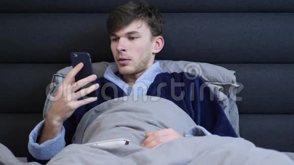 穿着浴衣的年轻人躺在床上睡前用智能手机看新闻男性躺在床上看着手机屏幕视频的预览图