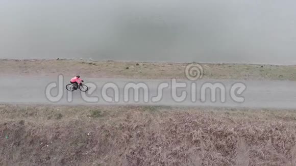 穿着职业运动装备的女人正沿着湖边骑着自行车骑自行车的人独自骑在靠近大坝的空步道上三径视频的预览图