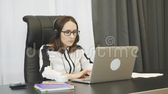 戴着耳机的女人和办公室里的伙伴聊天女商人戴着无线耳机手提电脑视频的预览图