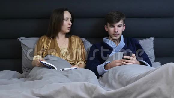 年轻的一家人躺在酒店房间里互相交谈一对相爱的夫妻在睡觉前躺在卧室里女人和男人撒谎视频的预览图