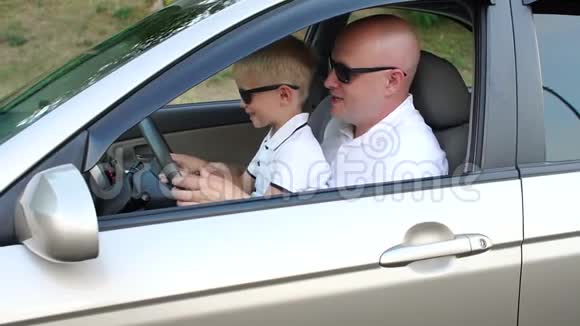 爸爸和儿子戴着墨镜在车里孩子学会了转动方向盘视频的预览图