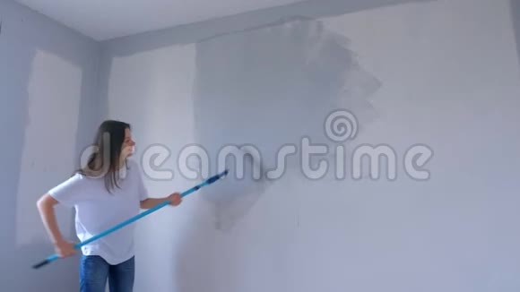 单身的年轻女子正在用新的平面上的油漆滚筒在灰色的墙壁上画画视频的预览图