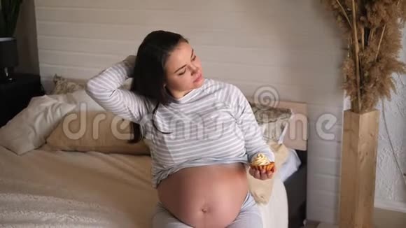 一个快乐微笑的怀孕女孩的肖像手里拿着一个蛋糕在床上视频的预览图