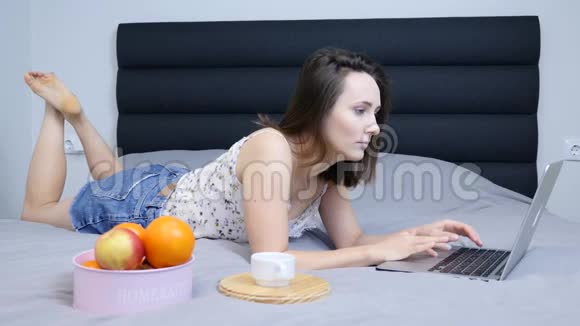 女千禧看着笔记本电脑屏幕躺在客厅的床上穿短裤的年轻女子在笔记本电脑上上网聊天视频的预览图