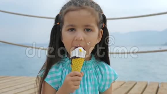 小女孩在大海或海洋的背景上舔冰淇淋锥视频的预览图