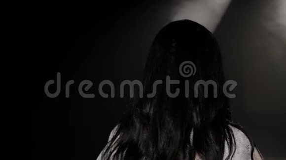 一个女人在黑暗中在白色聚光灯下上台的肖像视频的预览图
