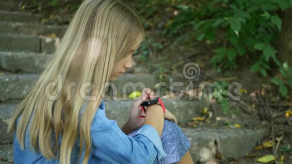 智能手表儿童使用智能手表儿童在智能手机交谈青少年女孩在公园户外浏览互联网视频的预览图