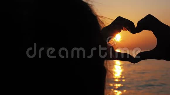 女孩在日落时的太阳背景上以心脏的形状牵手视频的预览图