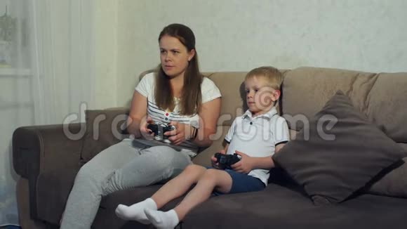 母子俩在家玩电子游戏一起坐在沙发上视频的预览图