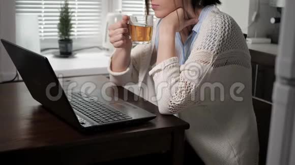 戴着眼镜和针织毛衣的可爱的白种人女孩在厨房里坐在公寓里喝着茶喝着茶视频的预览图
