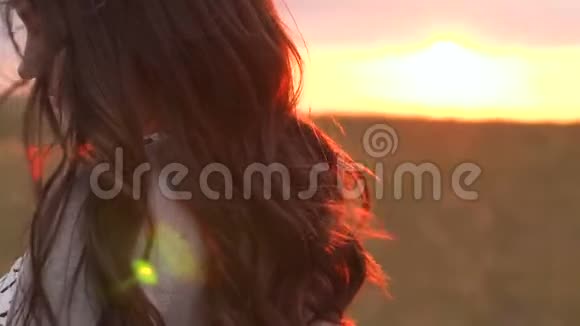 一个留着长发的女孩站在夕阳下的田野里视频的预览图