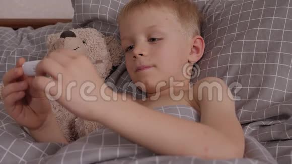 一个生病的小男孩躺在床上拿着温度计和泰迪熊视频的预览图