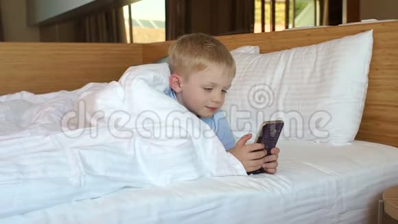 一个在家打电话的小男孩躺在毯子下面的床上视频的预览图
