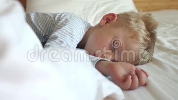 一个金发小男孩睡在一张白色的床上慢动作视频的预览图