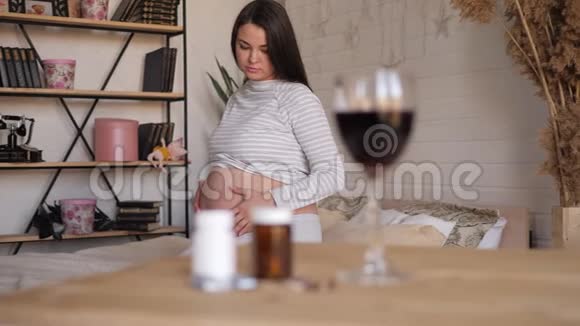 一杯酒和药丸放在桌上一位孕妇正坐在后台视频的预览图