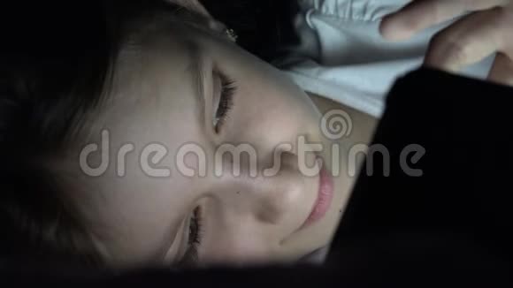 孩子在晚上玩平板电脑孩子在床上浏览互联网青少年女孩不能在黑暗中睡觉使用智能手机视频的预览图