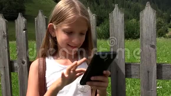 孩子玩智能手机孩子在平板电脑上浏览互联网青少年女孩在大自然中使用户外技术视频的预览图