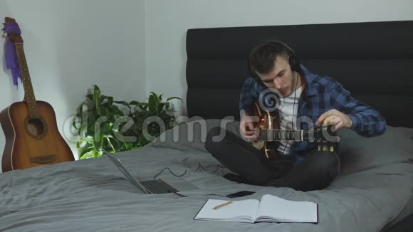 吉他老师调吉他弦戴耳机的年轻人在家里的床上调整电吉他有吉他的男音乐家视频的预览图