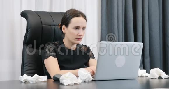 生病的女人在办公室里用笔记本电脑工作桌子上躺着脏餐巾纸有鼻涕的女性电脑打字员视频的预览图