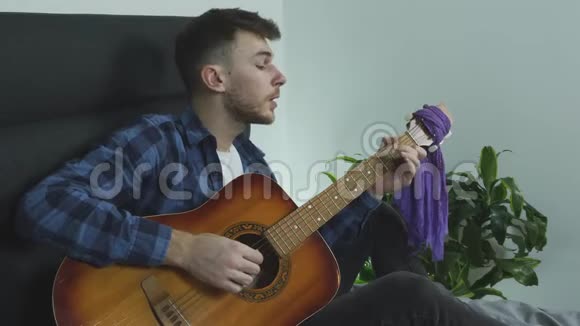 吉他音乐家用吉他演奏民谣歌曲并在家里床上有感情地唱歌视频的预览图