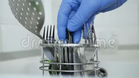 双手用橡胶手套清洗餐具并将其置于金属支架中视频的预览图