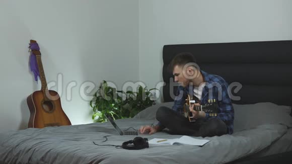 男人弹吉他摇滚年轻的音乐家坐在现代客厅的床上玩电吉他男性练习吉他视频的预览图