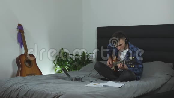 音乐家用电吉他创作新歌年轻的千禧一代在现代客厅的床上练习吉他男子演抒情剧视频的预览图