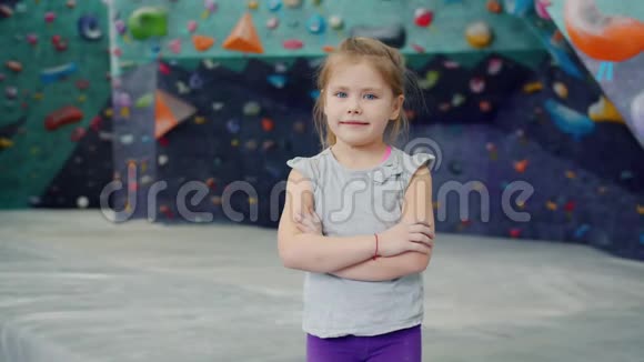 一个可爱的小女孩独自站在攀岩馆看镜头的肖像视频的预览图