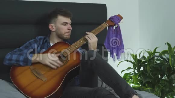 音乐作曲家在家里写一首歌坐在床上拿着一把吉他音乐概念视频的预览图