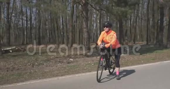 女的骑自行车肖像女人骑着自行车站在空路上的森林里骑自行车运动员准备骑自行车视频的预览图