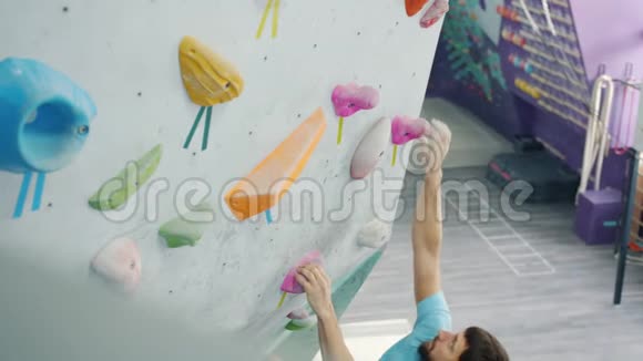 年轻男性成人在健身房攀爬明亮的人造墙的高角度视角视频的预览图