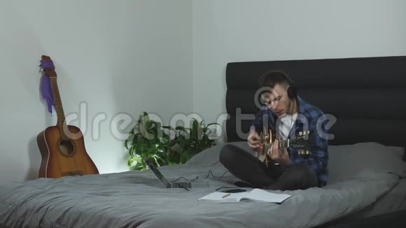 戴耳机的人用电吉他唱歌和演奏男音乐家在现代客厅的床上唱他的新歌吉他视频的预览图