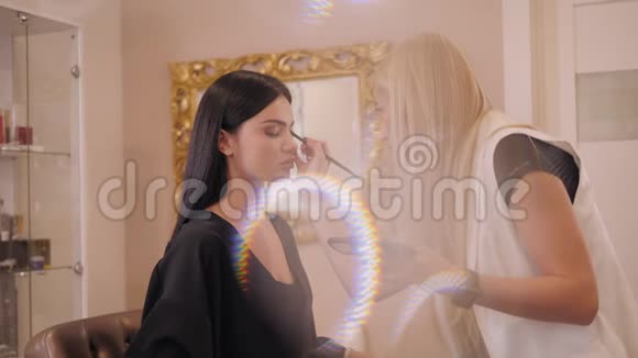 化妆师在沙龙与客户合作前景中模糊的灯光视频的预览图