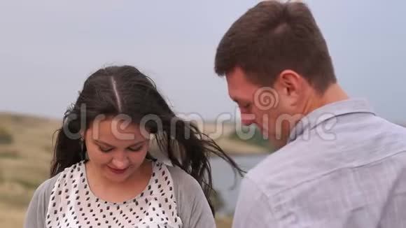 幸福的怀孕夫妇在湖边和田野的背景下走在户外视频的预览图