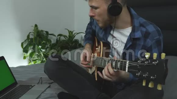 男人在笔记本电脑前弹吉他戴着耳机练习现场音乐会学习一首歌视频的预览图