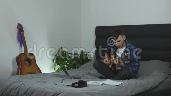 男性练习吉他年轻的白种人穿着潘通蓝色t恤正在现代家庭的床上学习电吉他音乐家视频的预览图