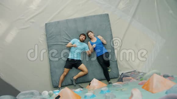 快乐的一对正在谈论攀岩的情侣躺在健身房的垫子上指着墙视频的预览图